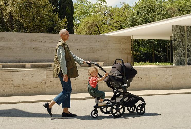 אישה הולכת עם תינוק בסלקל בוגבו טרטל אייר מולבש על מרכב פוקס 5 אליו מחובר גם בורד טרמפיסט עם פעוט ישוב עליו.